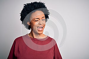 Young beautiful African American afro woman with curly hair wearing casual t-shirt standing winking looking at the camera with