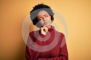 Young beautiful African American afro woman with curly hair wearing casual turtleneck sweater with hand on chin thinking about