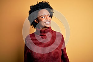 Young beautiful African American afro woman with curly hair wearing casual turtleneck sweater looking away to side with smile on