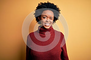 Young beautiful African American afro woman with curly hair wearing casual turtleneck sweater winking looking at the camera with