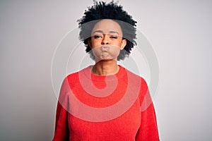 Young beautiful African American afro woman with curly hair wearing red casual sweater puffing cheeks with funny face