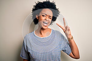 Young beautiful African American afro woman with curly hair wearing striped t-shirt smiling with happy face winking at the camera