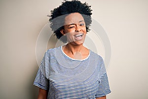 Young beautiful African American afro woman with curly hair wearing striped t-shirt winking looking at the camera with sexy