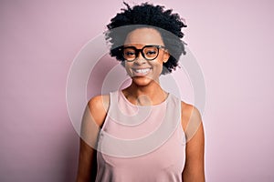 Young beautiful African American afro woman with curly hair wearing t-shirt and glasses with a happy and cool smile on face