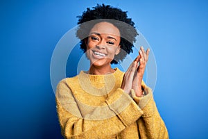 Young beautiful African American afro woman with curly hair wearing yellow casual sweater clapping and applauding happy and