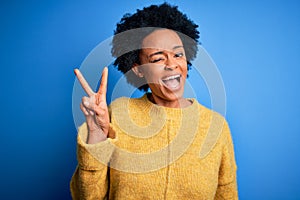 Young beautiful African American afro woman with curly hair wearing yellow casual sweater smiling with happy face winking at the
