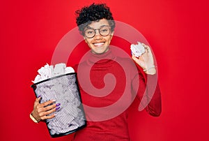 Young beautiful african american afro woman holding full paper bin with crumpled papers with a happy face standing and smiling