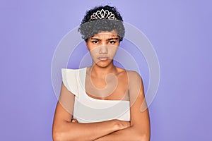 Young beautiful african american afro woman wearing tiara crown over purple background skeptic and nervous, disapproving
