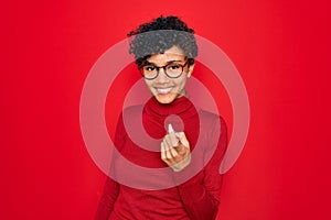 Young beautiful african american afro woman wearing turtleneck sweater and glasses Beckoning come here gesture with hand inviting