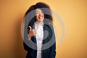 Young beautiful african american business woman with afro hair wearing elegant jacket doing happy thumbs up gesture with hand