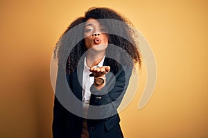 Young beautiful african american business woman with afro hair wearing elegant jacket looking at the camera blowing a kiss with