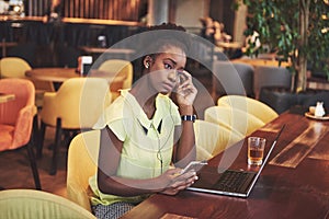 Young beautiful African-American business woman talking on the phone while working in a cafe