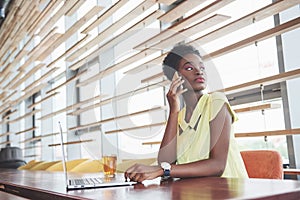 Young beautiful African-American business woman talking on the phone while working in a cafe