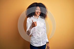 Young beautiful african american elegant woman with afro hair standing over yellow background doing happy thumbs up gesture with