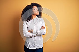 Young beautiful african american elegant woman with afro hair standing over yellow background looking to the side with arms