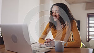 Young beautiful African American female happily working online from home on her laptop engaging in meeting video call