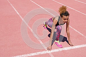 A young beautiful African American girl in a sporty black T-shirt and pink sneakers is preparing to race on the starting strip of