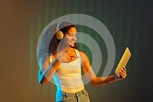 Young beautiful African-American girl using tablet  on light background.