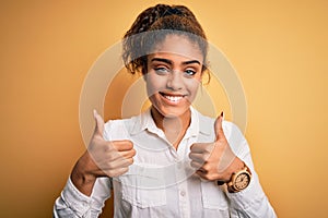 Young beautiful african american girl wearing casual shirt standing over yellow background success sign doing positive gesture