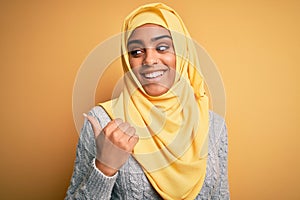 Young beautiful african american girl wearing muslim hijab over isolated yellow background smiling with happy face looking and