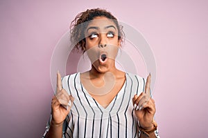 Young beautiful african american girl wearing striped t-shirt standing over pink background amazed and surprised looking up and