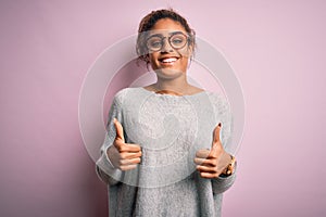 Young beautiful african american girl wearing sweater and glasses over pink background success sign doing positive gesture with