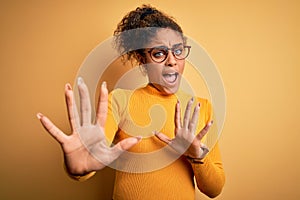 Young beautiful african american girl wearing sweater and glasses over yellow background afraid and terrified with fear expression