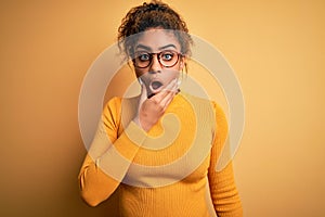 Young beautiful african american girl wearing sweater and glasses over yellow background Looking fascinated with disbelief,