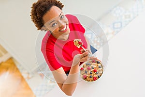 Young beautiful african american woman with afro hair eating healthy wholemeal cereals and berries as healthy breakfast