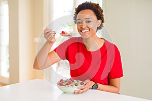 Young beautiful african american woman with afro hair eating healthy wholemeal cereals and berries as healthy breakfast