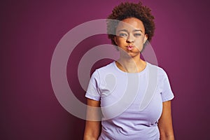 Young beautiful african american woman with afro hair over isolated purple background puffing cheeks with funny face