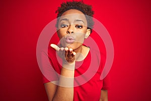 Young beautiful african american woman with afro hair over isolated red background looking at the camera blowing a kiss with hand