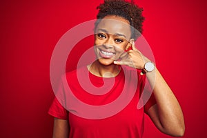 Young beautiful african american woman with afro hair over isolated red background smiling doing phone gesture with hand and