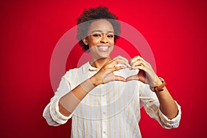 Young beautiful african american woman with afro hair over isolated red background smiling in love showing heart symbol and shape