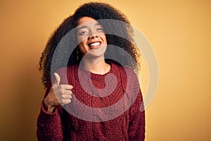 Young beautiful african american woman with afro hair standing over yellow isolated background doing happy thumbs up gesture with