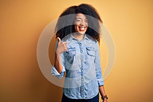 Young beautiful african american woman with afro hair standing over yellow isolated background doing happy thumbs up gesture with