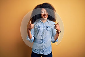 Young beautiful african american woman with afro hair standing over yellow isolated background success sign doing positive gesture