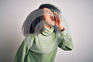 Young beautiful african american woman with afro hair wearing green winter sweater shouting and screaming loud to side with hand