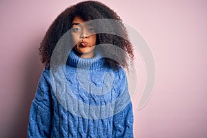 Young beautiful african american woman with afro hair wearing winter sweater over pink background puffing cheeks with funny face