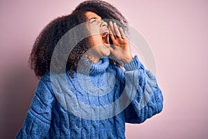 Young beautiful african american woman with afro hair wearing winter sweater over pink background shouting and screaming loud to