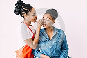 Young beautiful African American woman applying professional make-up by African make-up artist. Studio shoot