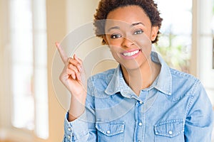 Young beautiful african american woman with a big smile on face, pointing with hand and finger to the side looking at the camera