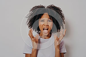 Young beautiful African American woman with curly hair standing angry and mad, raising hands up