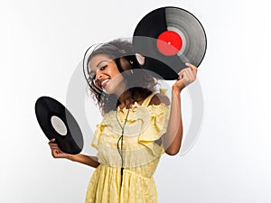 Young beautiful african american woman with headphones in yellow dress enjoying and dancing with vinyl records at white
