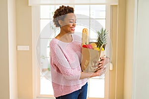 Young beautiful african american woman holding paper bag full of fresh healthy groceries