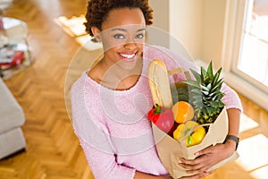 Young beautiful african american woman holding paper bag full of fresh healthy groceries