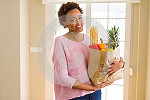 Young beautiful african american woman holding paper bag full of fresh healthy groceries