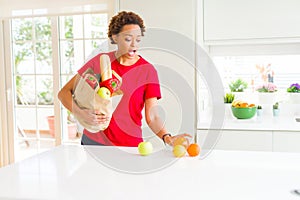 Young beautiful african american woman holding paper bag full of fresh healthy groceries leaving vegetables on the table