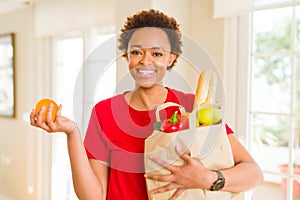 Young beautiful african american woman holding paper bag full of fresh healthy groceries and picking vegetables