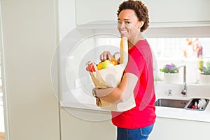 Young beautiful african american woman holding paper bag full of fresh healthy groceries and picking vegetables